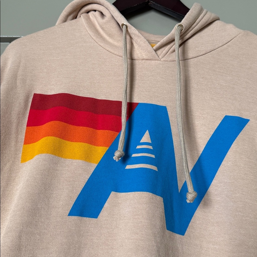 Aviator Nation Beige Hoodie with Blue AV Logo and Red‑Orange‑Yellow Wave